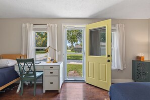 A bedroom with a bed, a desk, a chair, and a door leading to a balcony.