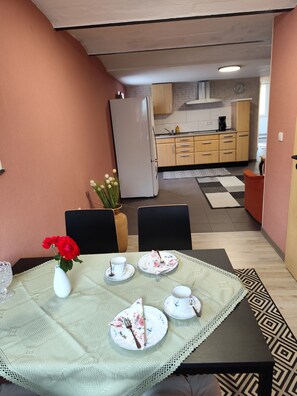 Ein Essbereich mit einem Tisch für zwei Personen, einer Vase mit roten Blumen und einer Küche im Hintergrund.