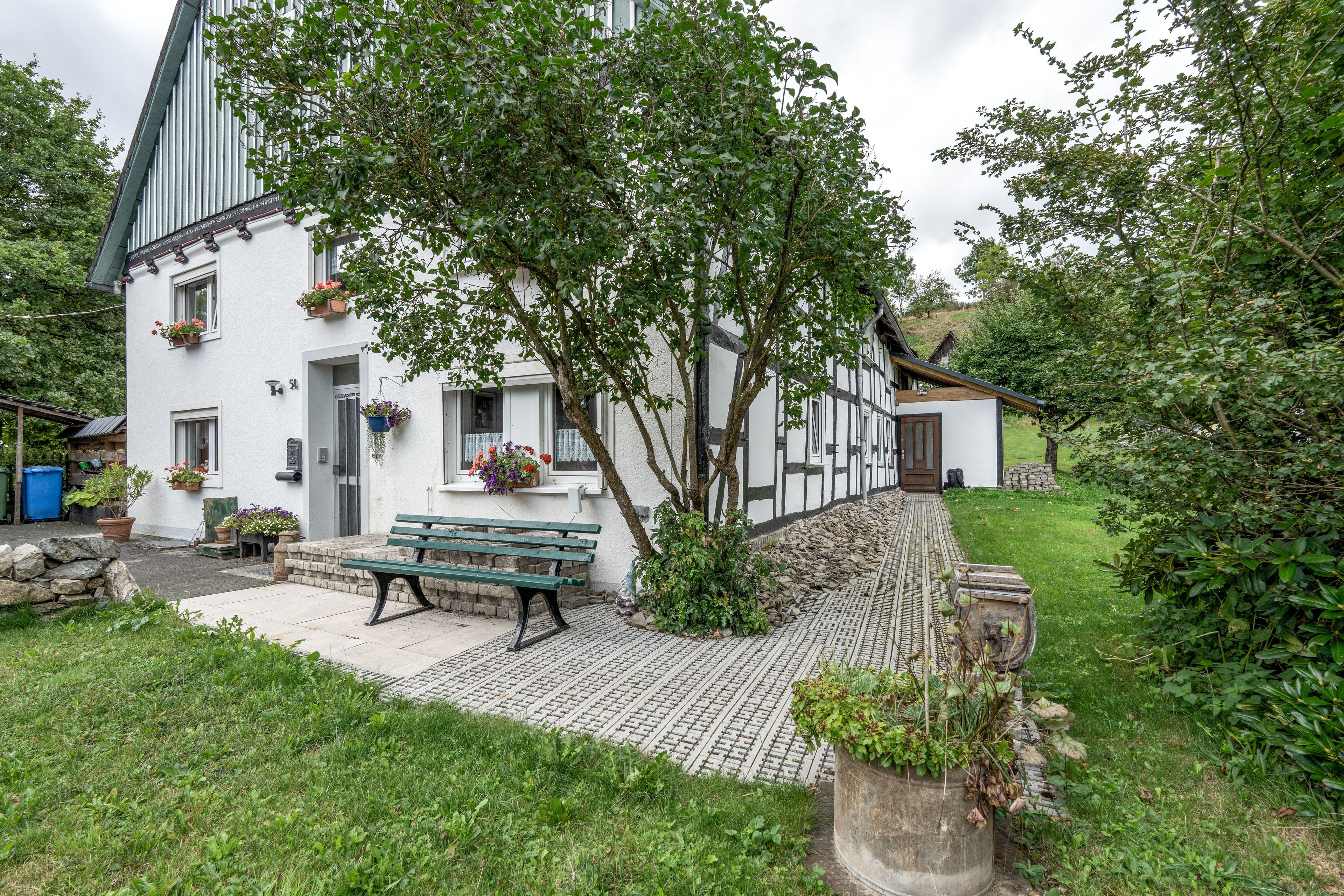 A traditional half-timbered house with a stone pathway leading to a bench.