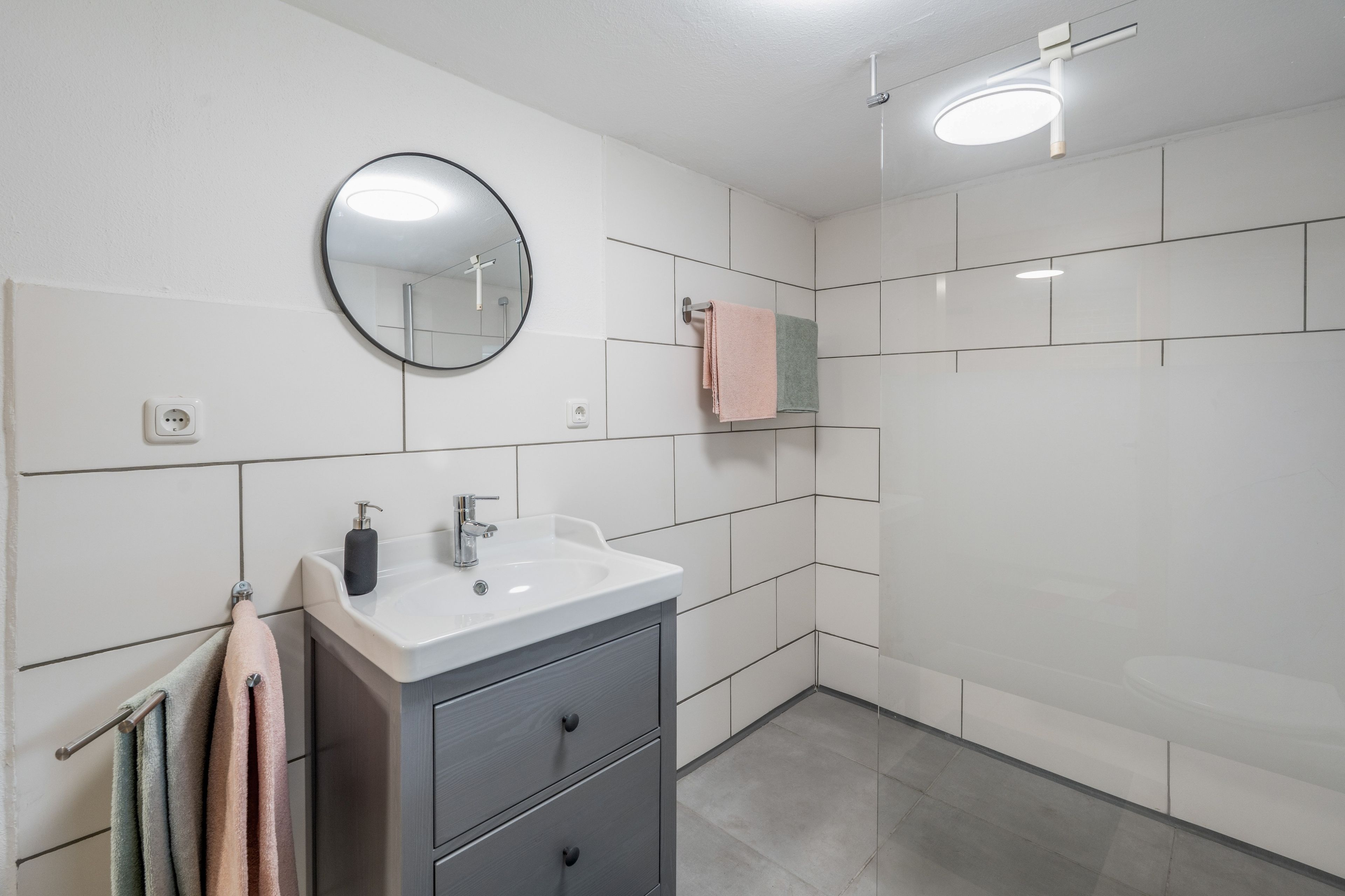 Une salle de bain moderne avec un lavabo blanc, un miroir et un porte-serviettes.