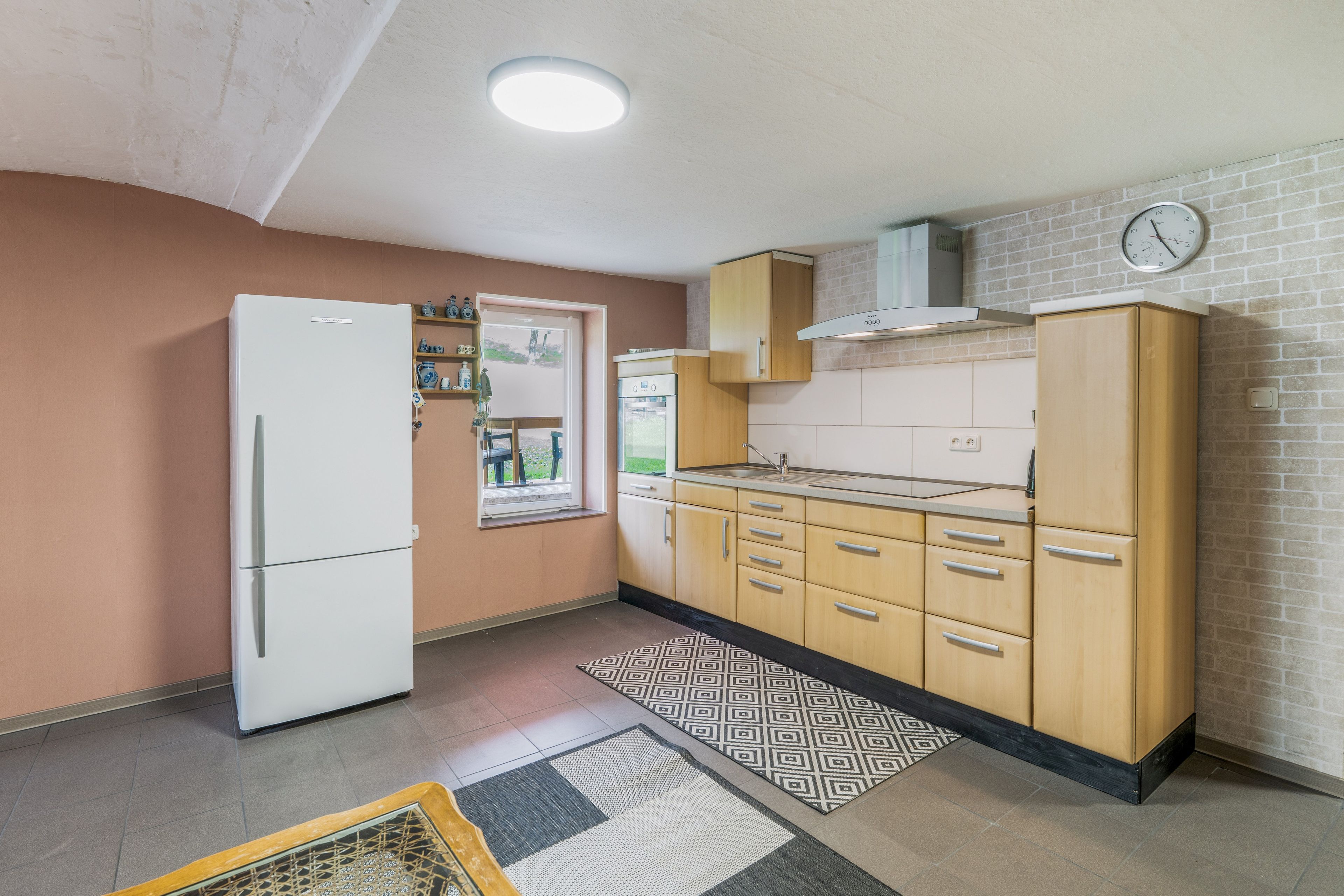 Eine kompakte Küche mit Kühlschrank, Holzschränken, einer Spüle und einer Uhr an der Wand.