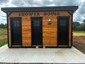 A wooden structure labeled 'SHOWER HOUSE' with three black doors and a small sign above the right door.