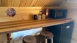 A wooden interior with a kitchen area, including a microwave, a refrigerator, and two stools.