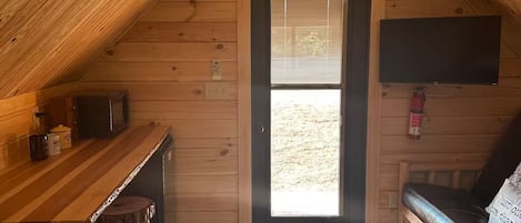 Quarto de sótão aconchegante com teto de madeira, pequena cozinha e um sofá.