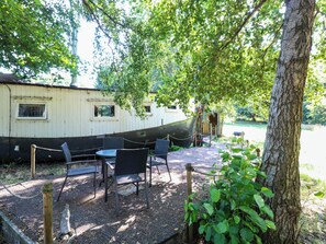 A boat house with a dining area featuring tables and chairs, surrounded by greenery. - Ladies of Bolton (Norwich)