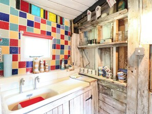 A kitchen with a colorful tiled backsplash, a wooden cabinet, and a shelf with various kitchen items. - Ladies of Bolton (Norwich)