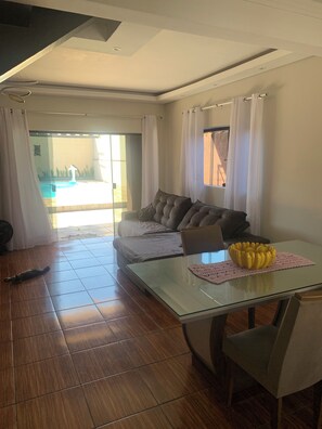 Ein modernes Wohnzimmer mit Glastisch, einer Couch und Blick auf einen Pool.