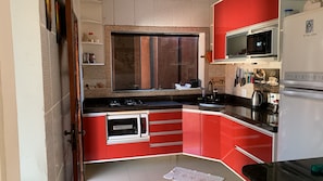 A compact kitchen with red cabinetry, a microwave, a stove, and a refrigerator. - Cozy house on the coast, family atmosphere, pets allowed. (Caraguatatuba)