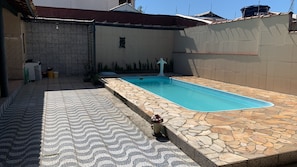 A swimming pool with a tiled deck, a wall with a decorative pattern, and a small statue. - Cozy house on the coast, family atmosphere, pets allowed. (Caraguatatuba)