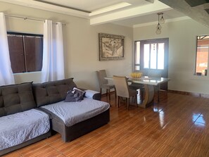 A living room with a sofa, a dining table with chairs, a painting on the wall, and a window with curtains. - Cozy house on the coast, family atmosphere, pets allowed. (Caraguatatuba)