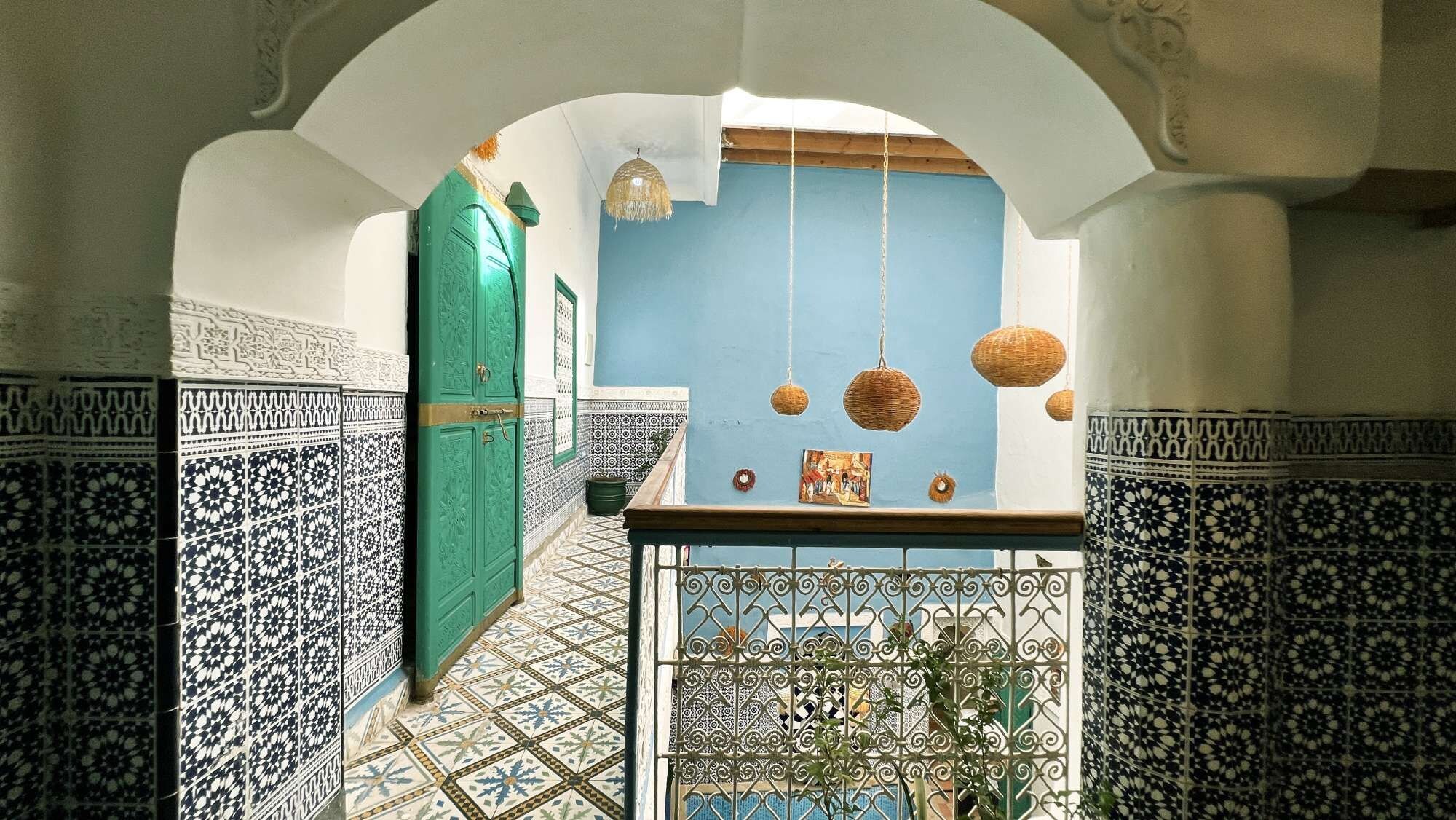 An interior corridor with patterned tiles, a green door, and hanging baskets.
