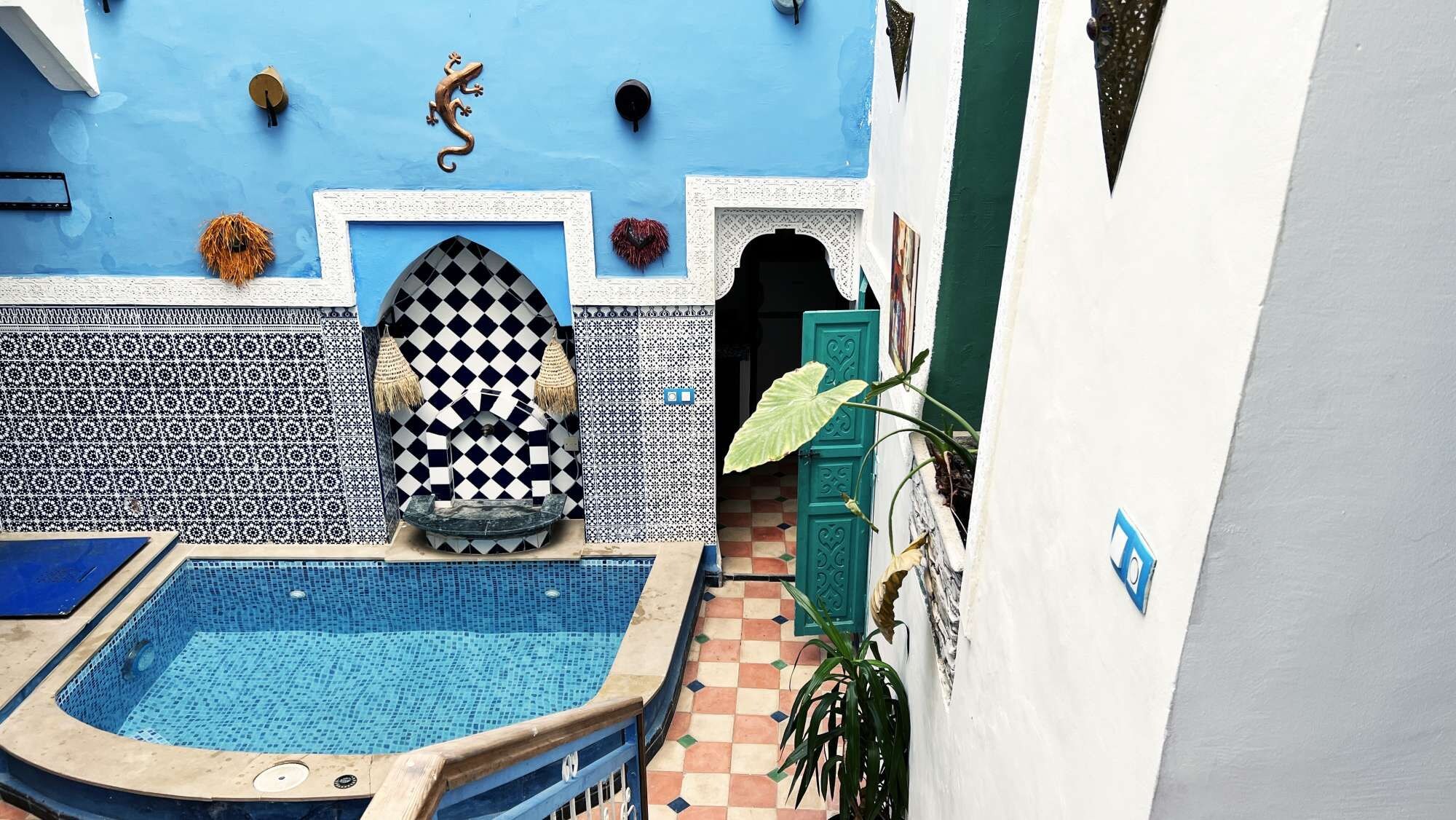 A pool area with a checkered wall, a blue pool, and a door leading to a covered entrance.