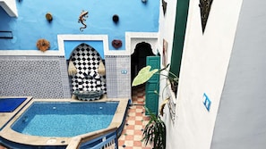 Ein Poolbereich mit einer Schachbrettwand, einem blauen Pool und einer Tür, die zu einem überdachten Eingang führt.