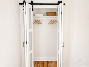 A white closet with a sliding door, wooden hangers, and a basket. - Luxe CLT City Stays -1 (Charlotte)