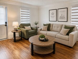 Uma sala de estar com sofá, poltrona, mesa de centro, abajur e quadros nas paredes.