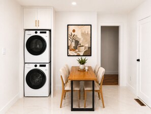 Cozinha moderna com máquina de lavar e secar integradas, mesa de jantar de madeira com cadeiras e uma obra de arte emoldurada na parede.