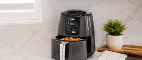 Une cuisine équipée d’un appareil de cuisson à air chaud Ninja noir, d’un plan de travail en marbre, d’un évier en acier inoxydable, d’une planche à découper en bois et d’une plante en pot.