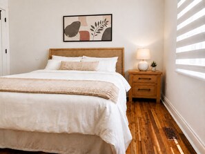Quarto com cama, mesa de cabeceira, abajur e um quadro na parede.