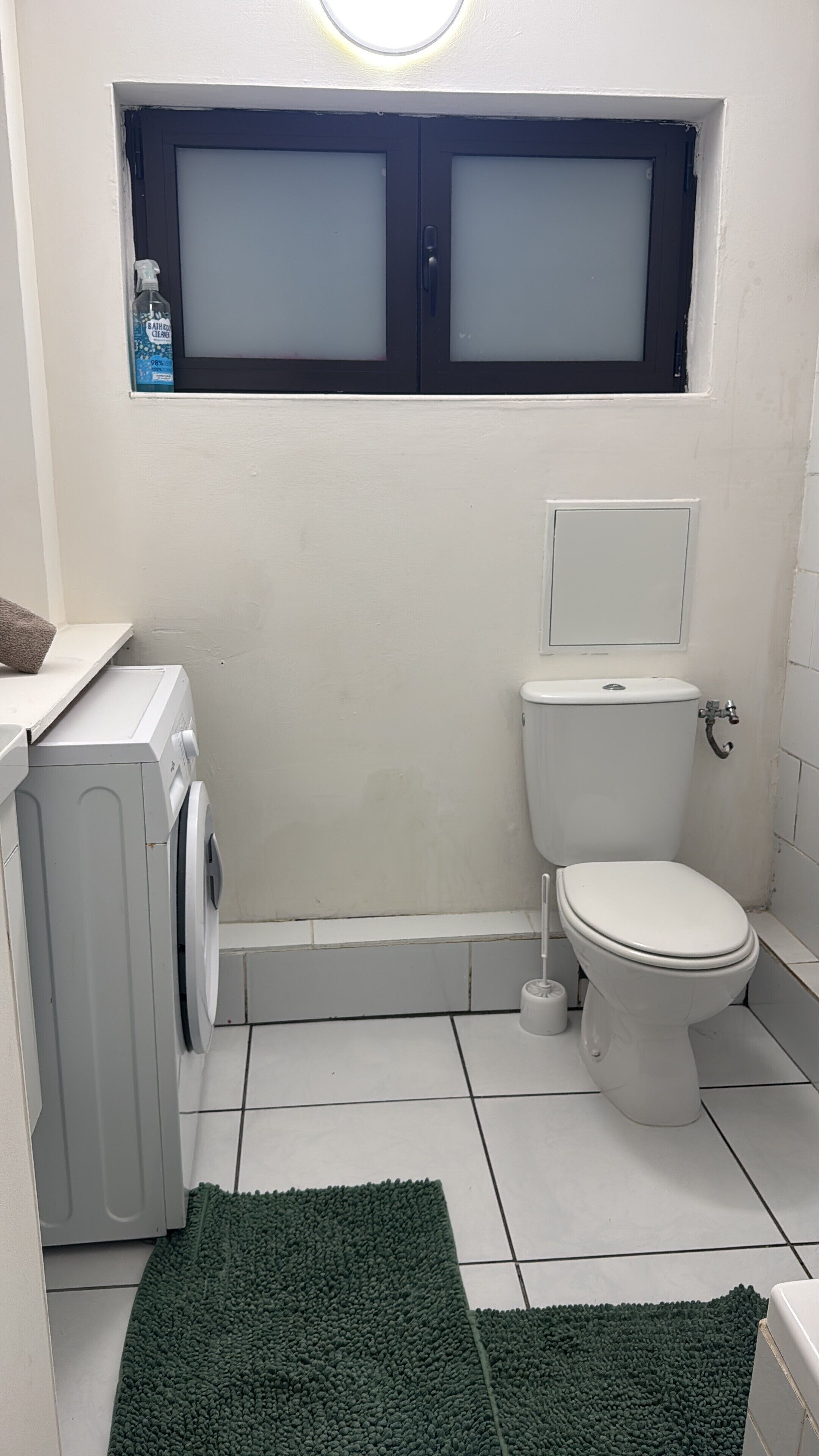 Een compacte badkamer met toilet, wasmachine en een klein raam boven de wastafel.