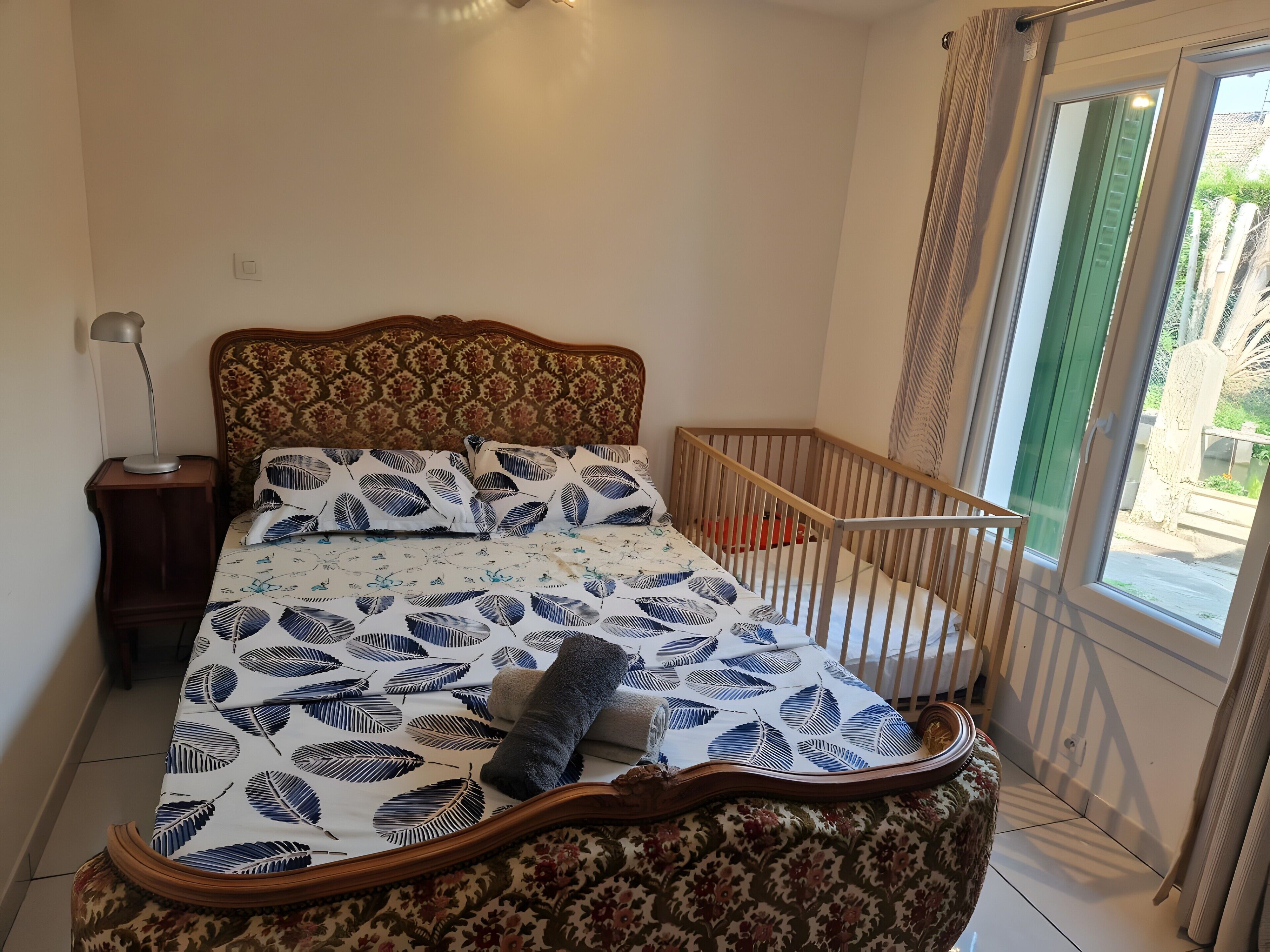 Une chambre à coucher avec un lit, une table de chevet, un berceau et une fenêtre avec des rideaux.