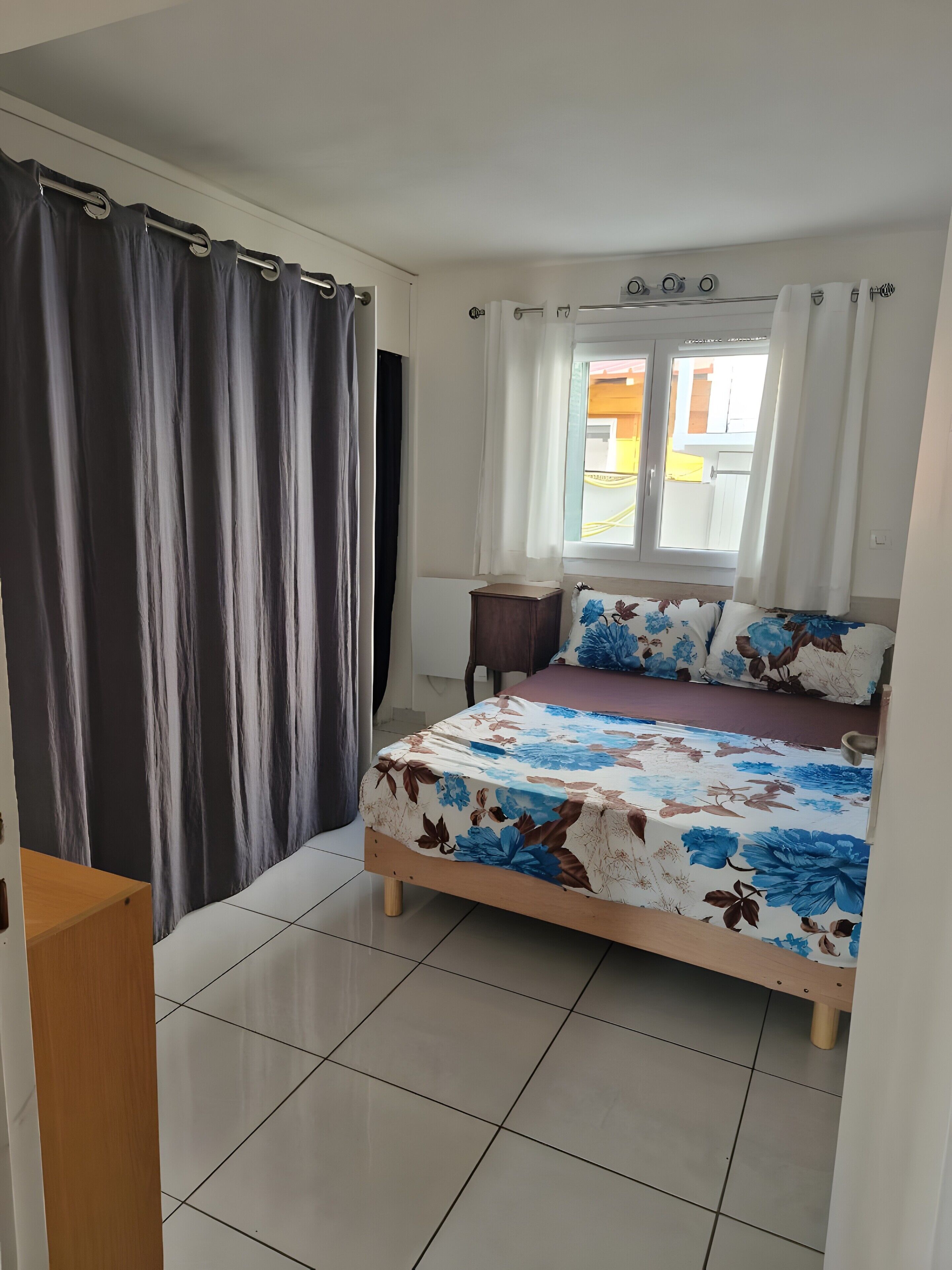 A bedroom with a bed, curtains, a window, and a tiled floor.