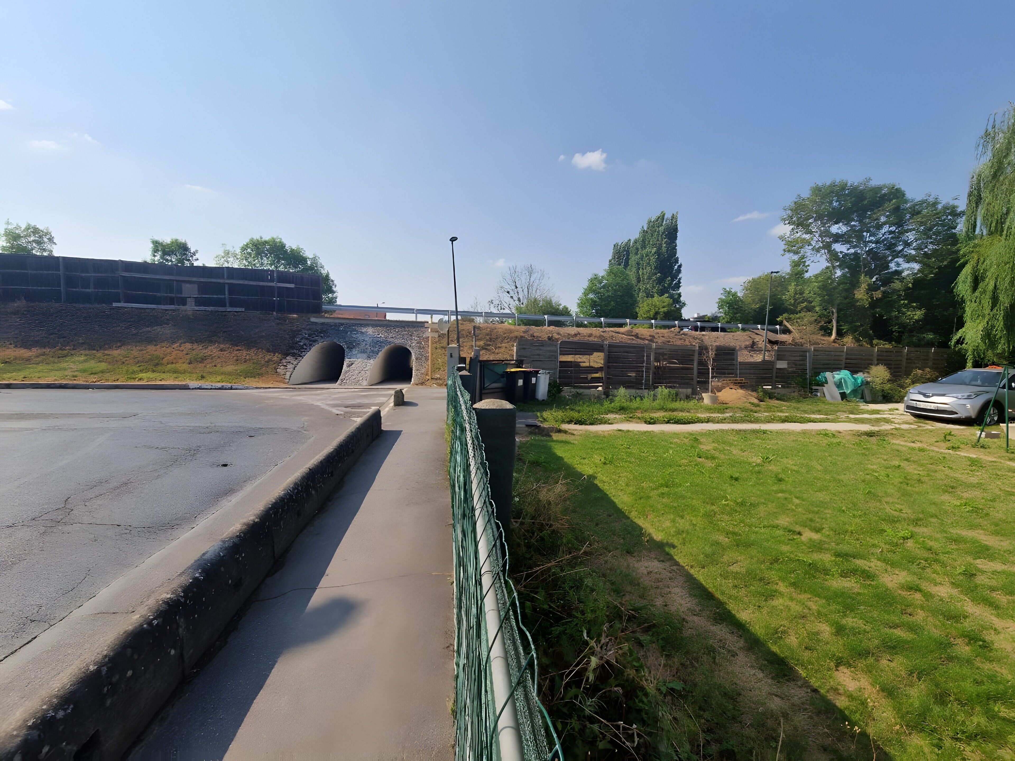 Een geplaveid pad dat naar de ingang van een tunnel leidt, een gazon met een hek, en een geparkeerde auto.