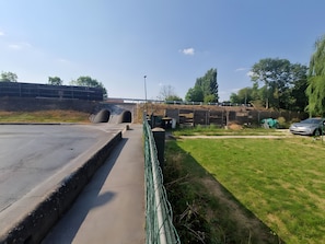 Un chemin pavé menant à l’entrée d’un tunnel, une zone herbeuse délimitée par une clôture et une voiture garée.