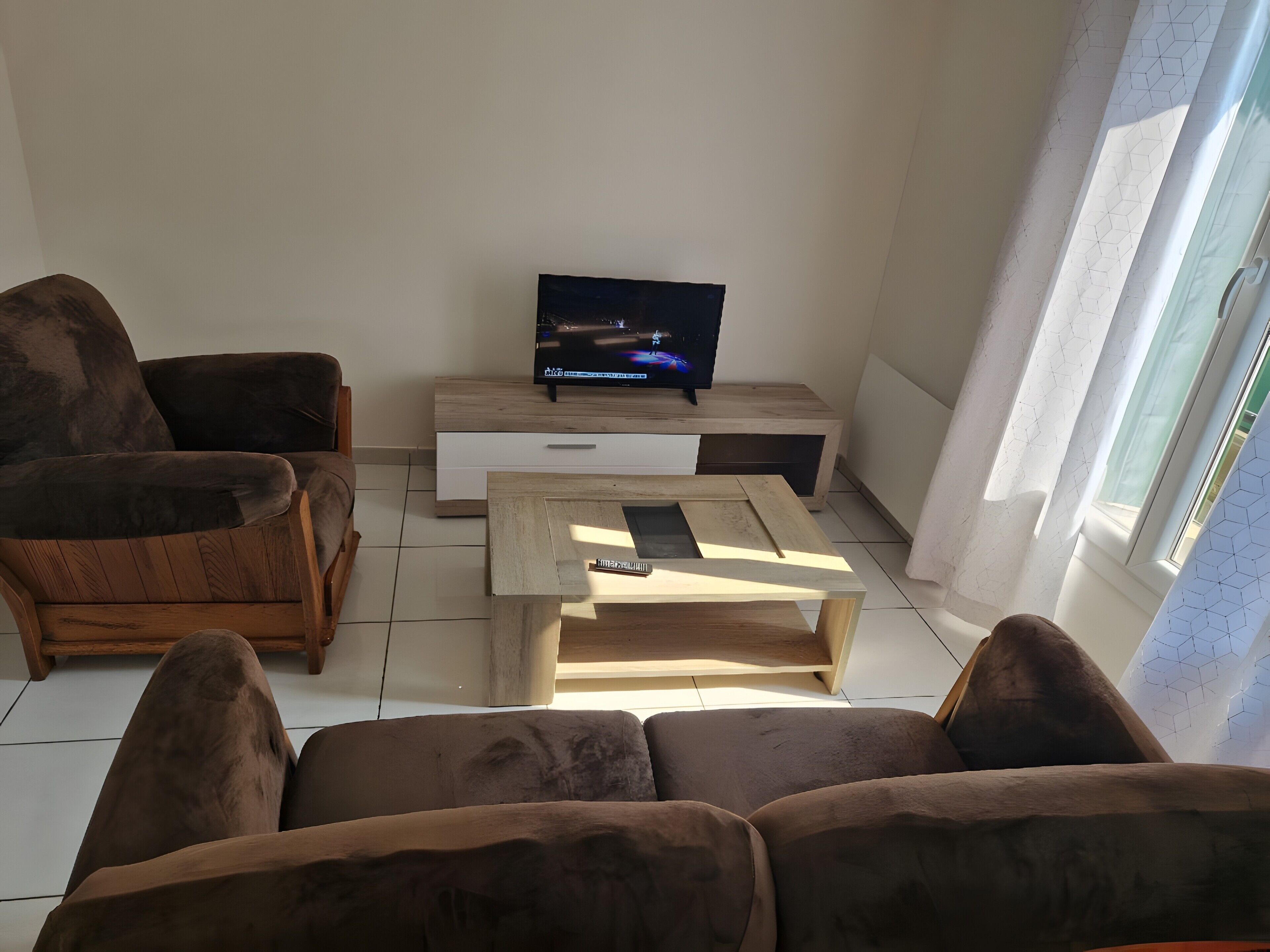 A living room with a sofa, a coffee table, a TV on a stand, and a window with curtains.