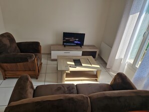 A living room with a sofa, a coffee table, a TV on a stand, and a window with curtains.