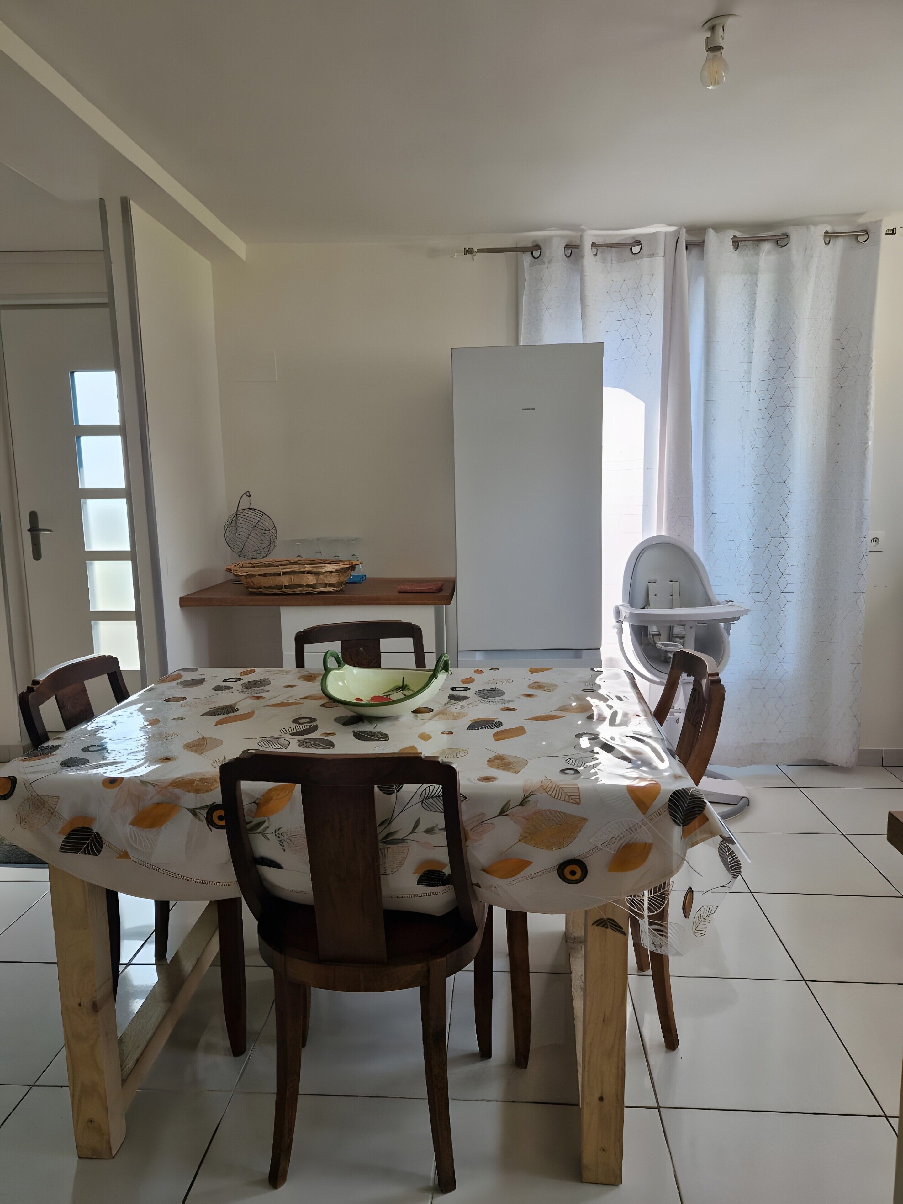A dining area with a table covered in a patterned tablecloth, surrounded by wooden chairs.