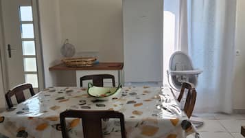 A dining area with a table covered in a patterned tablecloth, surrounded by wooden chairs.