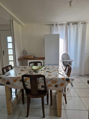 A dining area with a table covered in a patterned tablecloth, surrounded by wooden chairs. - Apartment 'One-story  with Garden' (Étampes)