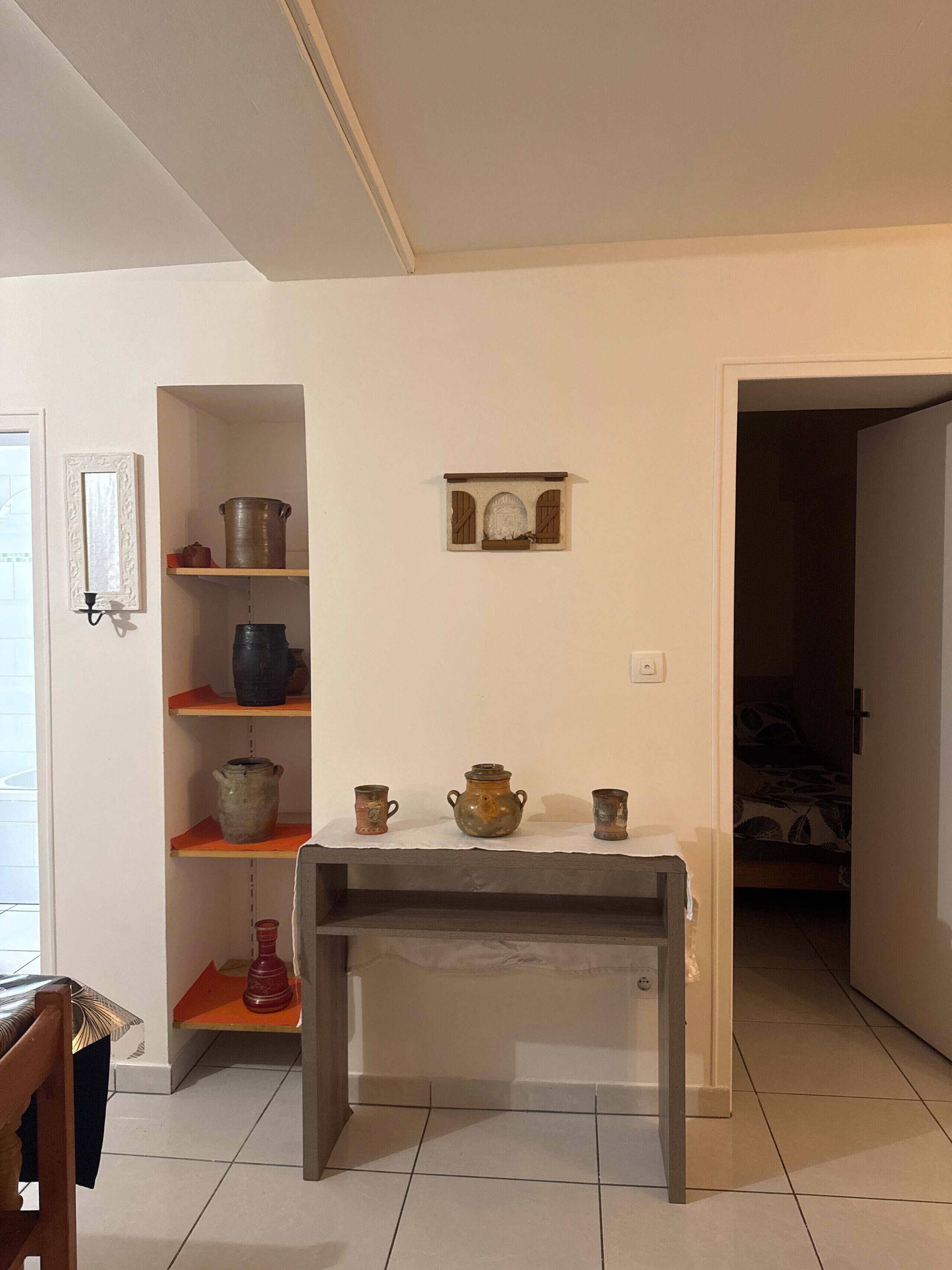 Une pièce avec un mur blanc, une petite table et une étagère sur laquelle se trouvent divers objets.