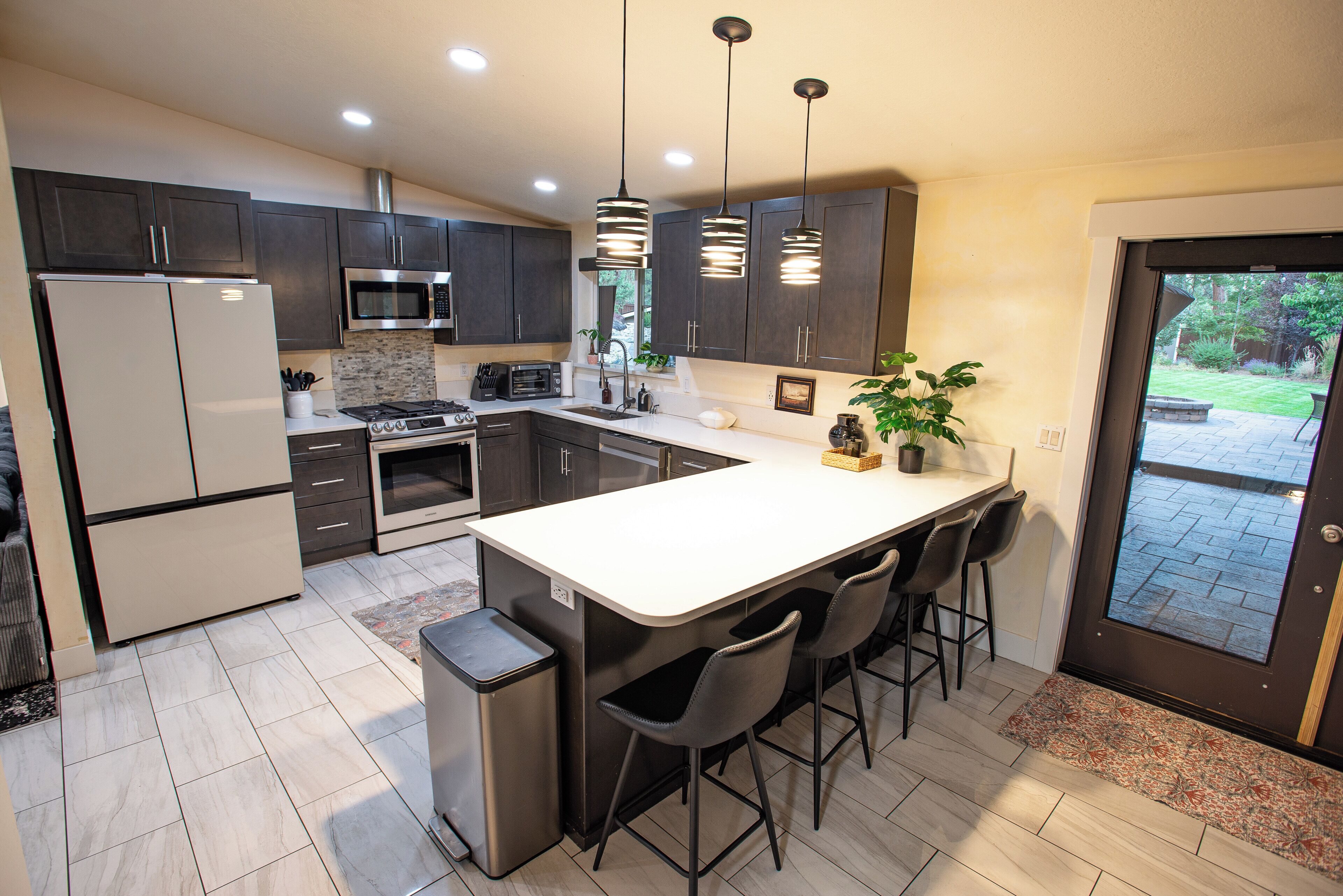 A modern kitchen with dark cabinets, stainless steel appliances, and a central island with bar stools.