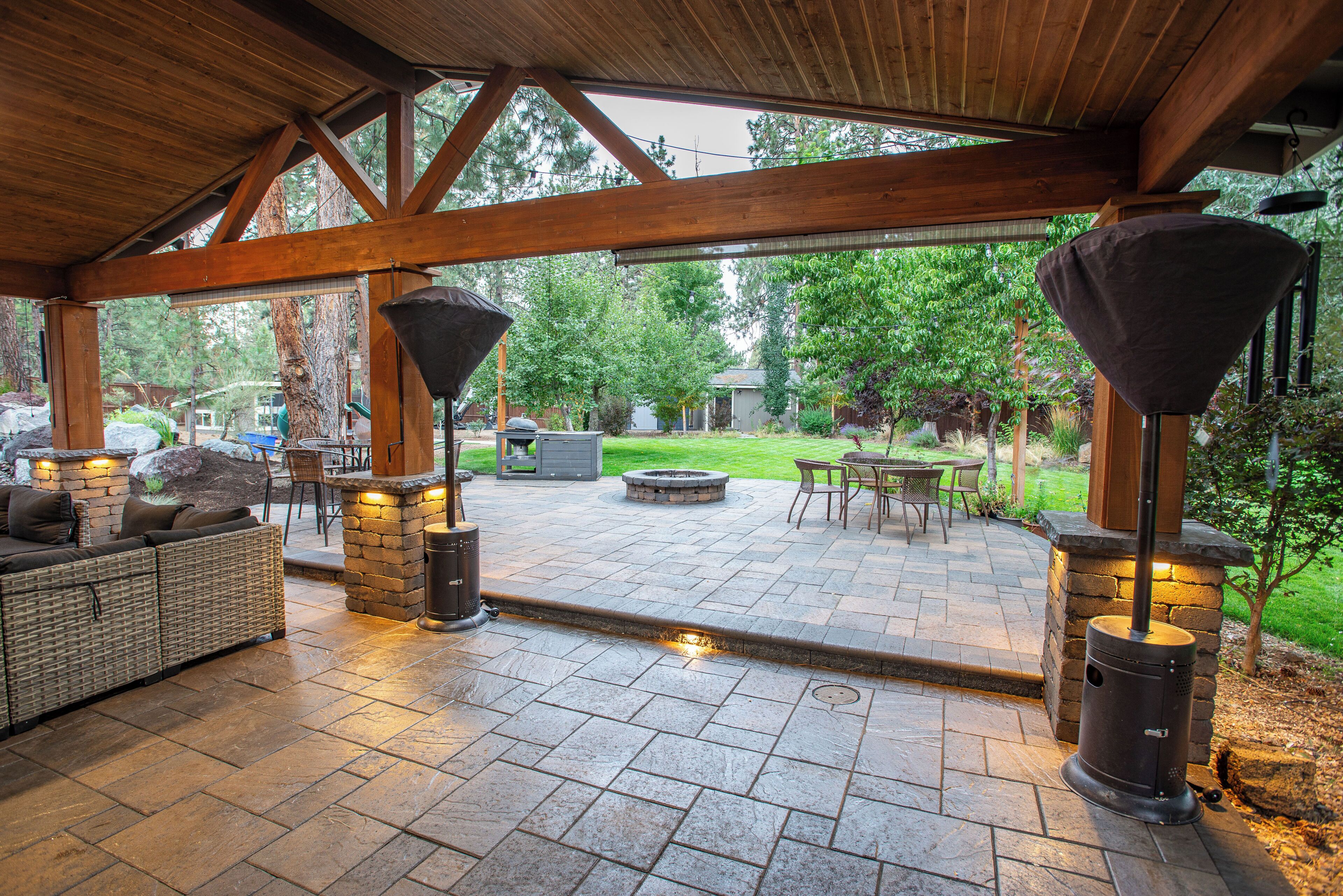 An outdoor patio with stone flooring, a seating area with wicker furniture, and a barbecue grill.