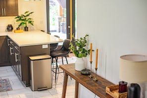 Eine moderne Küche mit einer zentralen Kochinsel, Barhocker, einem kleinen Kühlschrank und einem Esstisch mit Kerzen und einer Vase.