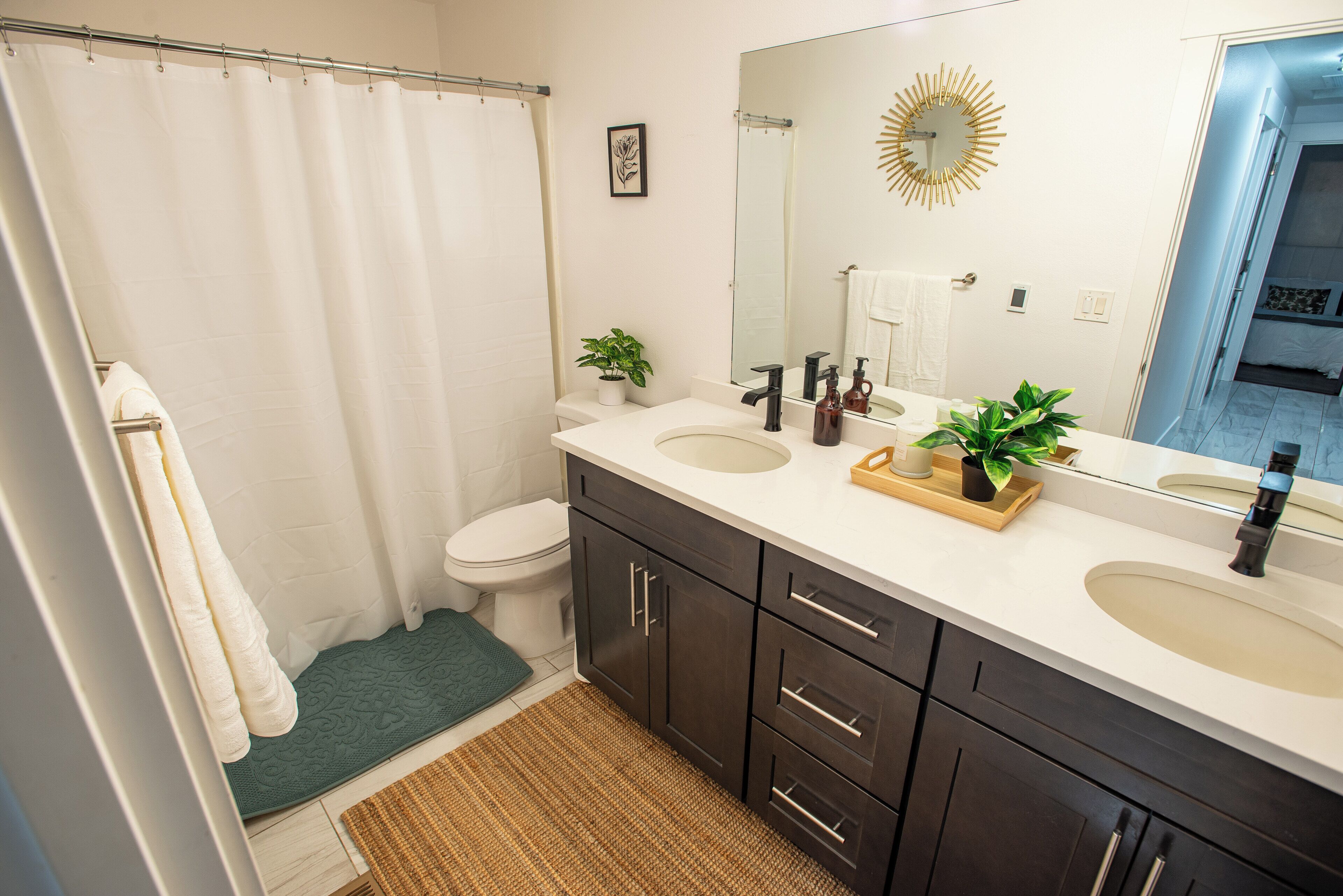 Une salle de bain avec un rideau de douche, des toilettes, un lavabo avec un miroir et une petite plante en pot.