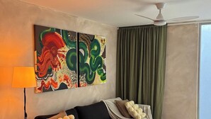 En moderne stue med en sort sofa, et tæppe, et maleri, en lampe og en loftventilator.