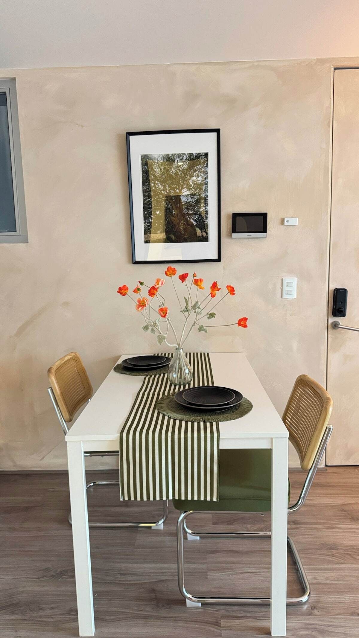 Et spiseområde med et hvidt bord, stribet dug og en vase med orange blomster.