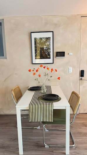 Ein Essbereich mit einem weißen Tisch, einer Streifen-Tischdecke und einer Vase mit orangenen Blumen.