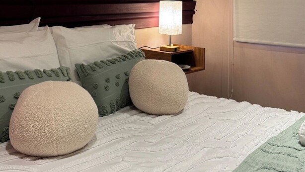 Et hotelværelse med en seng, puder, et natbord med lampe, et vindue med rullegardin og en væg med struktur.
