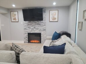 Una sala de estar con chimenea, un televisor de pantalla plana montado encima y un sofá con cojines.