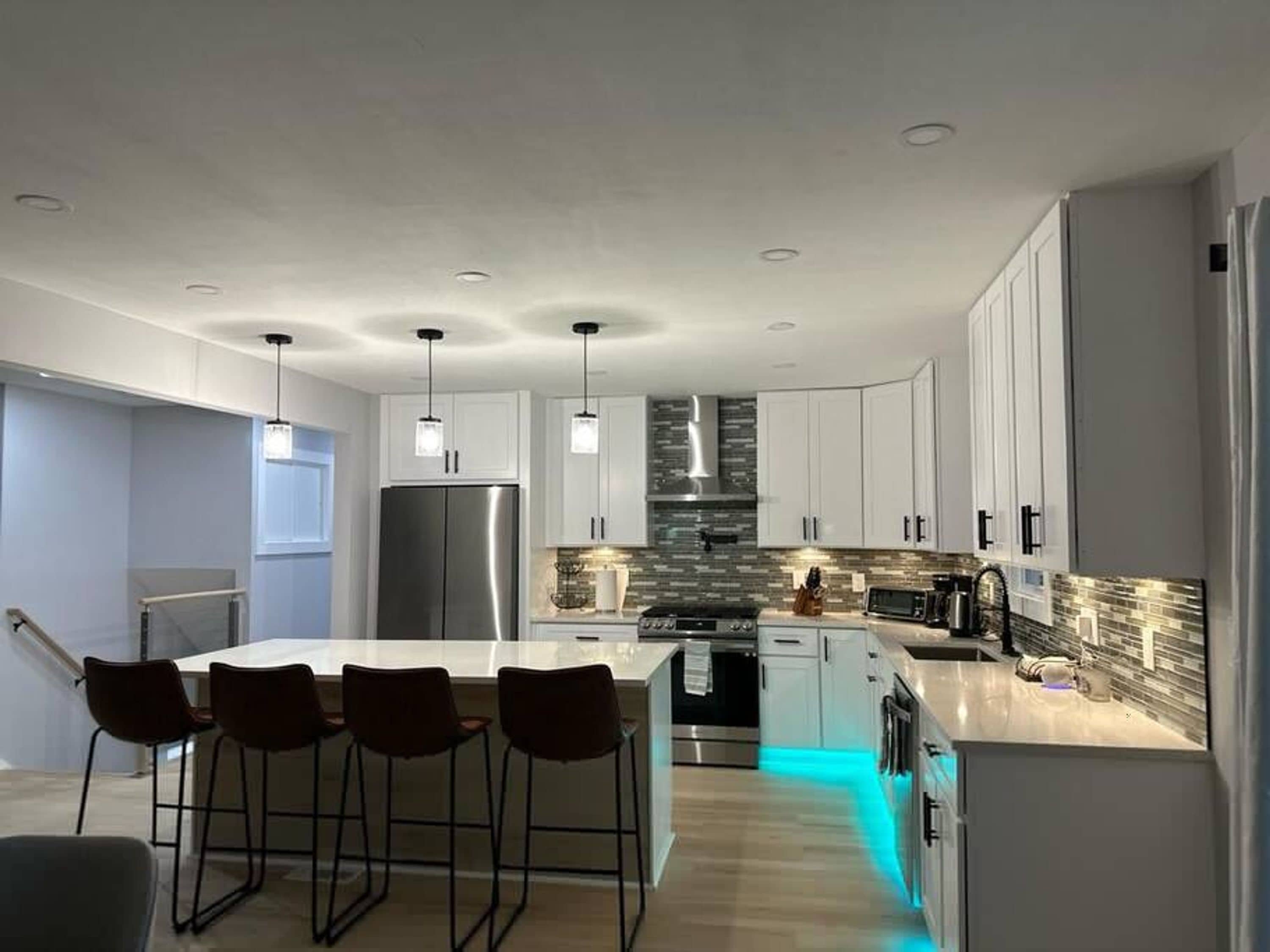 A modern kitchen with a central island, bar stools, stainless steel appliances, and pendant lighting.