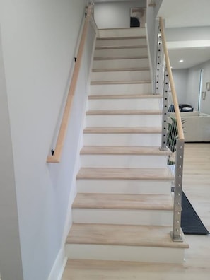 A staircase with wooden steps and metal handrails, leading to a landing with a black mat. - Urban Xcape- Family Vibe With Plush Amenities (Silver Spring)