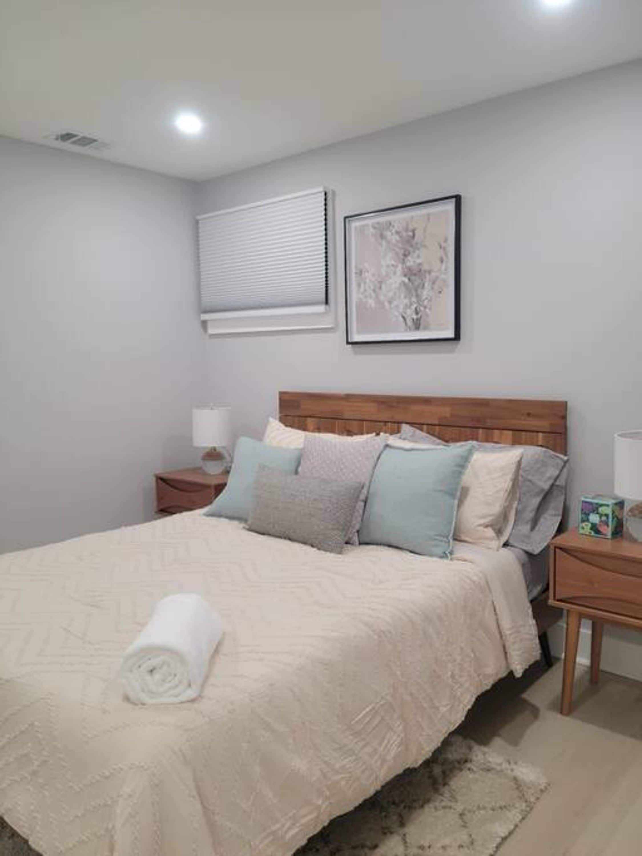 A neatly made bed with a rolled white towel, a wooden headboard, and a bedside table with a lamp.