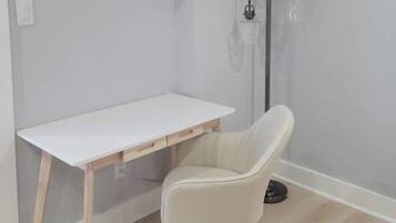 A room with a white desk, a white chair, and a floor lamp with two bulbs.