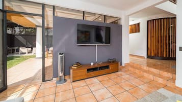 A modern living room with a flat-screen TV mounted on a wall, a wooden entertainment unit below, and a large glass door leading to an outdoor area.