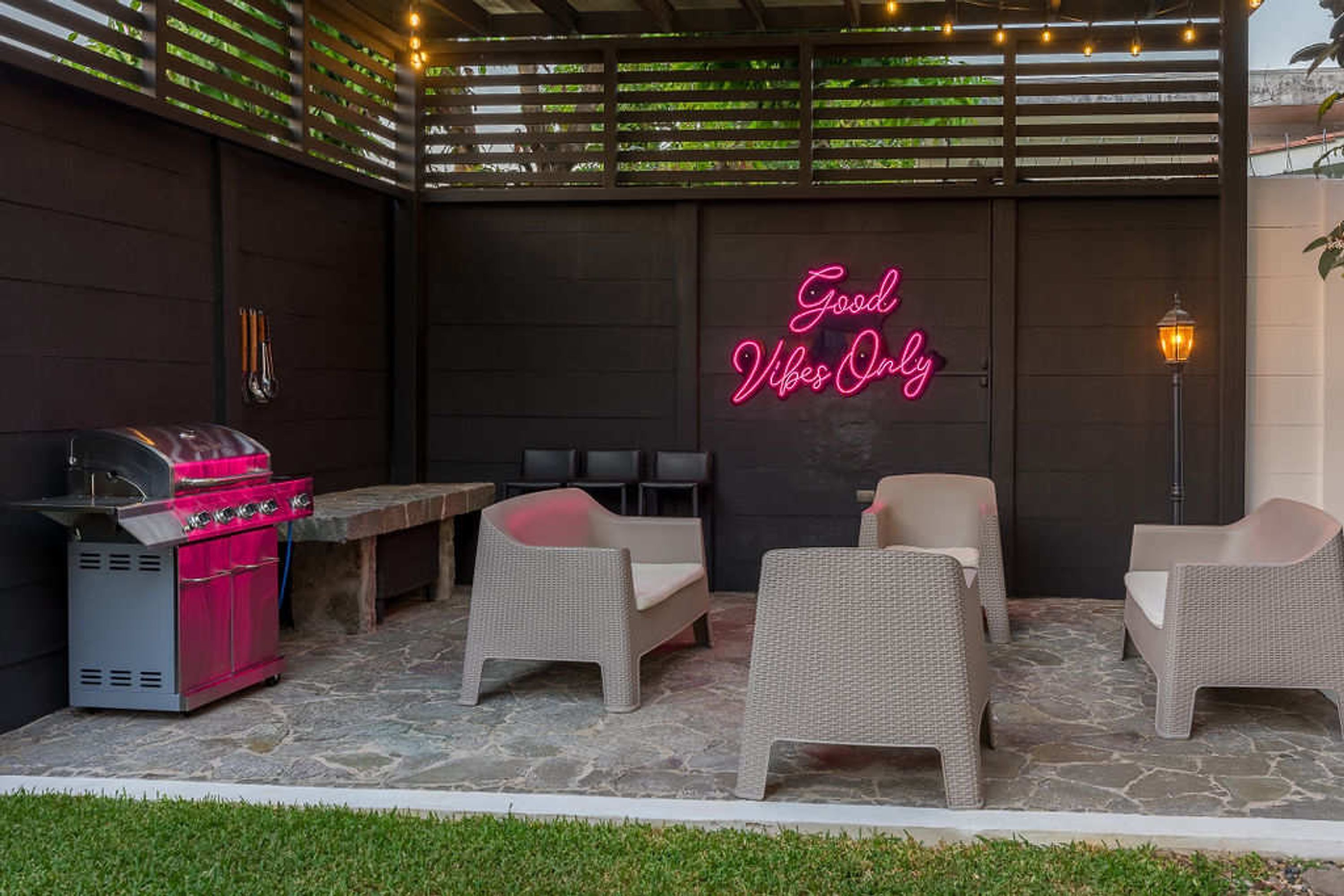 Une terrasse extérieure avec des meubles en osier, un barbecue et un panneau lumineux au néon.