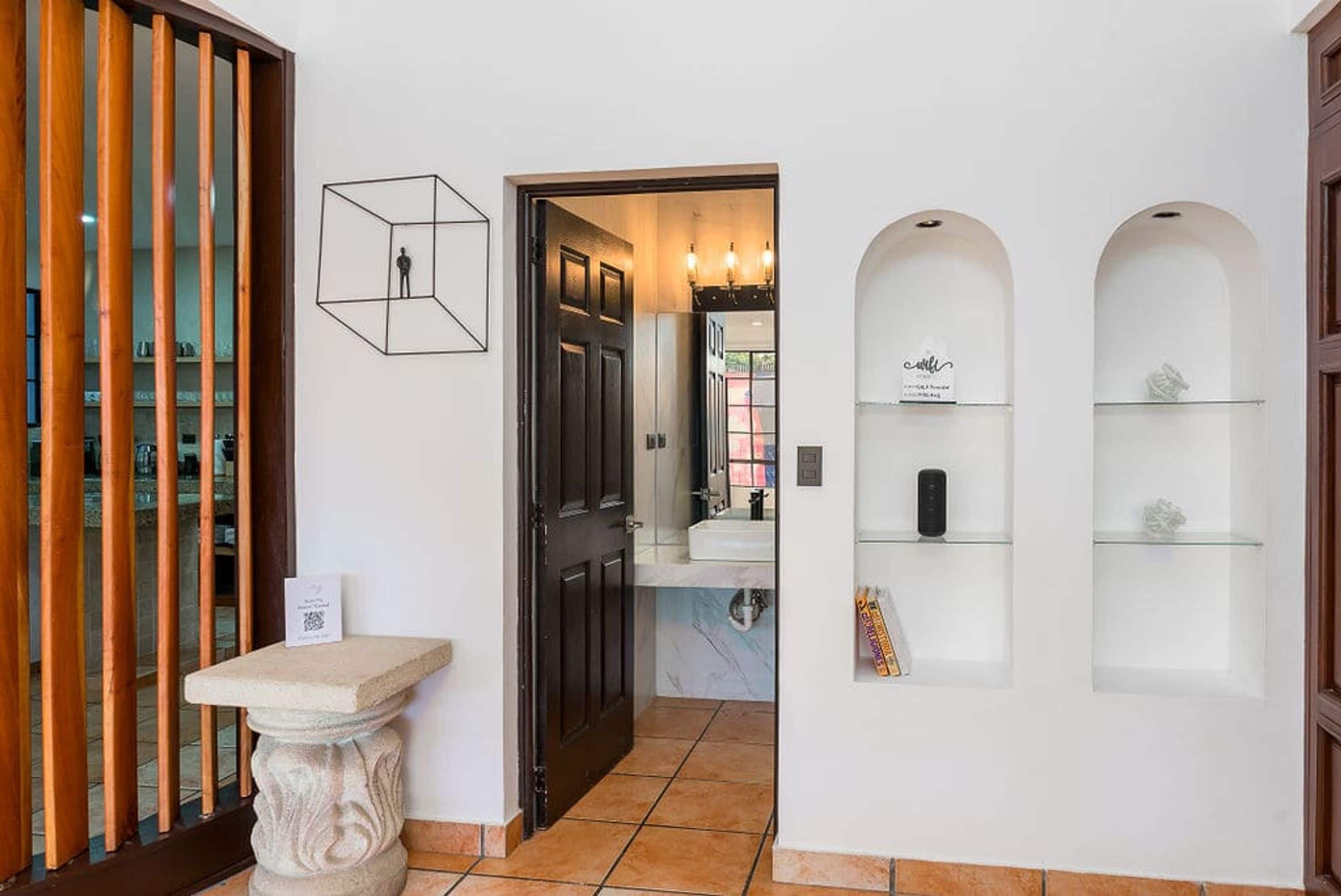 A hallway with a stone pedestal, a black door, and a white wall with shelves.