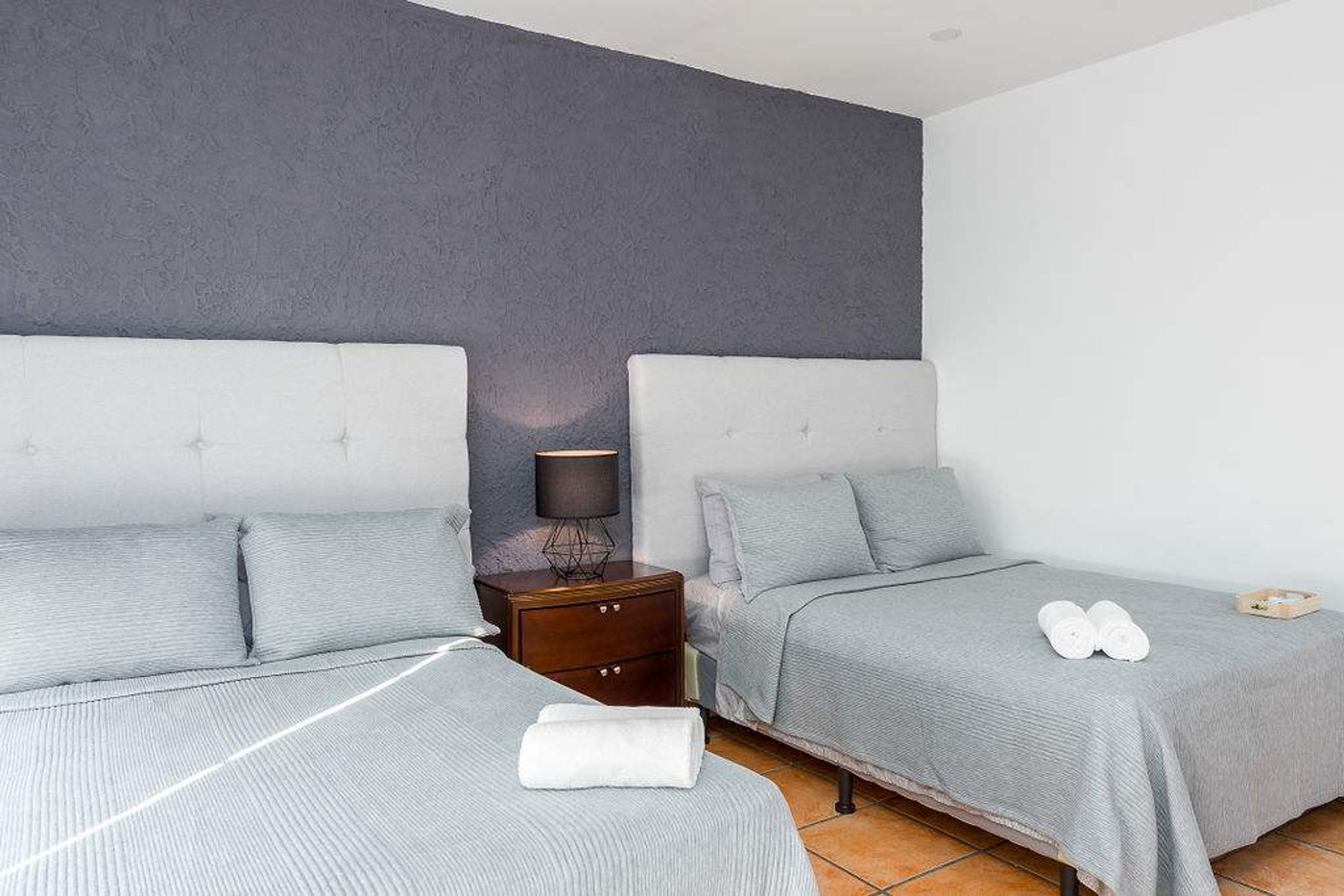 A hotel room with two beds, a nightstand with a lamp, and a pair of towels on the floor.